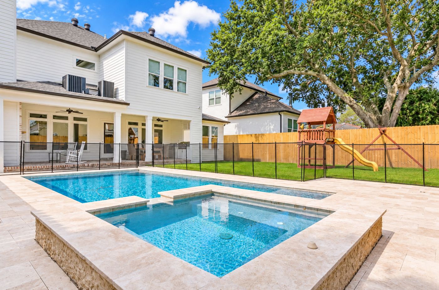 Rectangular gunite pool with a raised spa and travertine deck behind a two-story white home