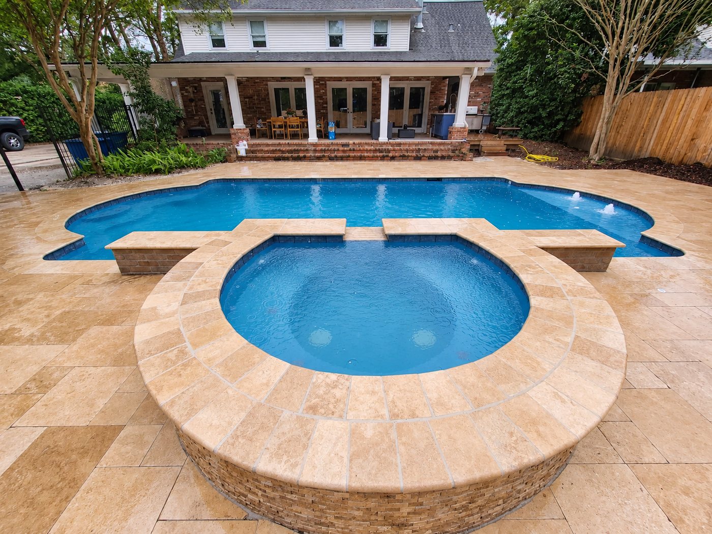 Raised round spa spilling into a gunite pool, with a travertine deck
