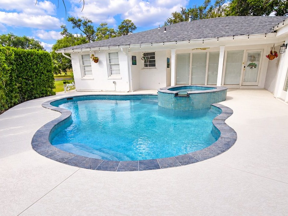 After: the same pool with a new coated deck, dark tile edge, and glass-tile spa