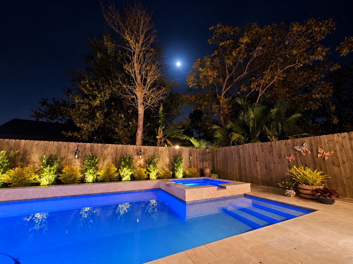 Pool and raised spa glowing blue at night under a full moon