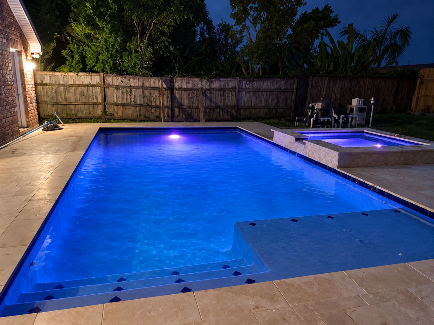 Rectangular pool with sun shelf and raised spa, lit at night