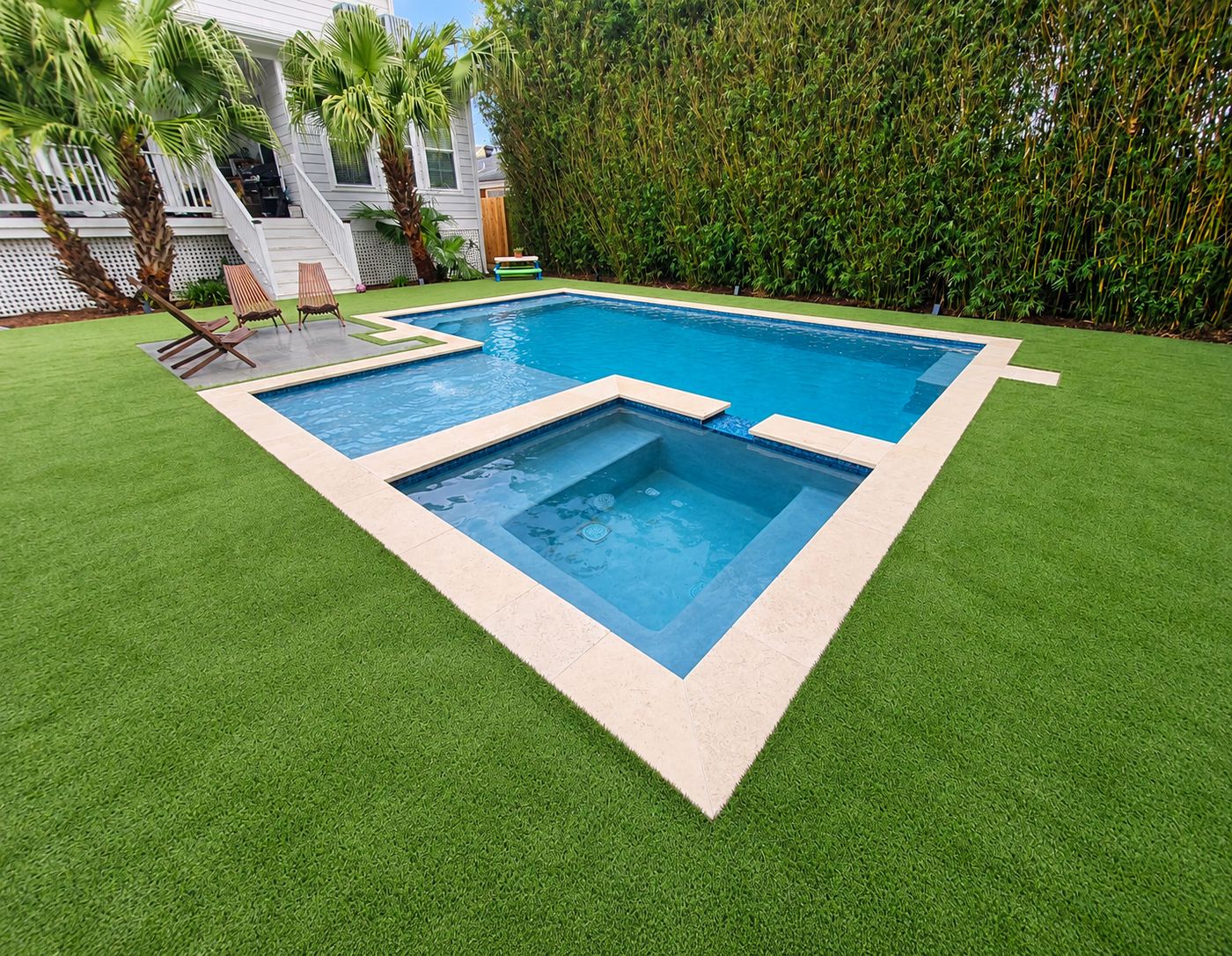 Geometric pool and in-ground spa with stone coping, set in artificial turf beside a white raised home